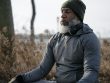Bearded African American male in warm activewear and knitted hat sitting and meditating with closed eyes in autumn nature